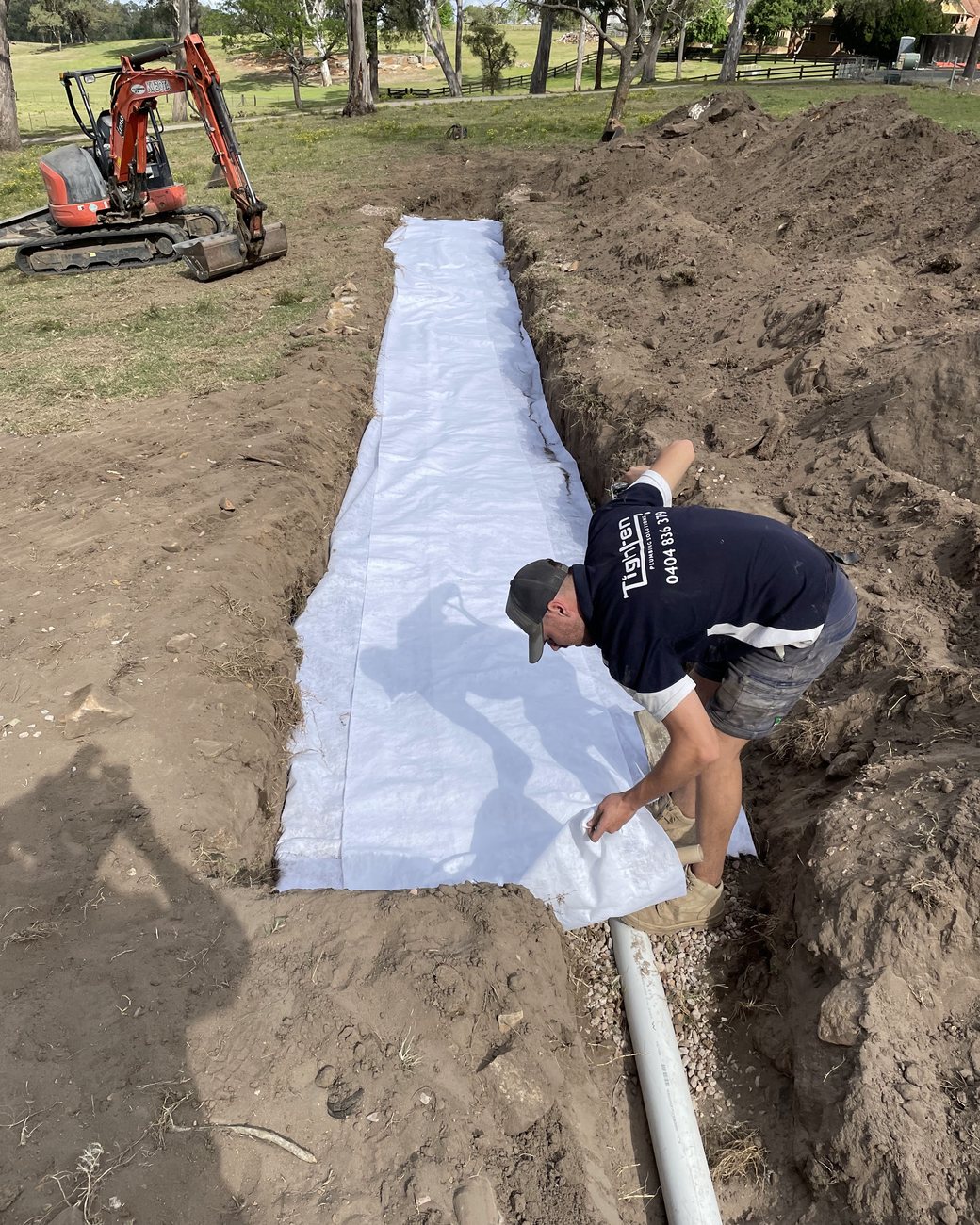 Tighten Plumbing Solutions worker laying drainage in a trench